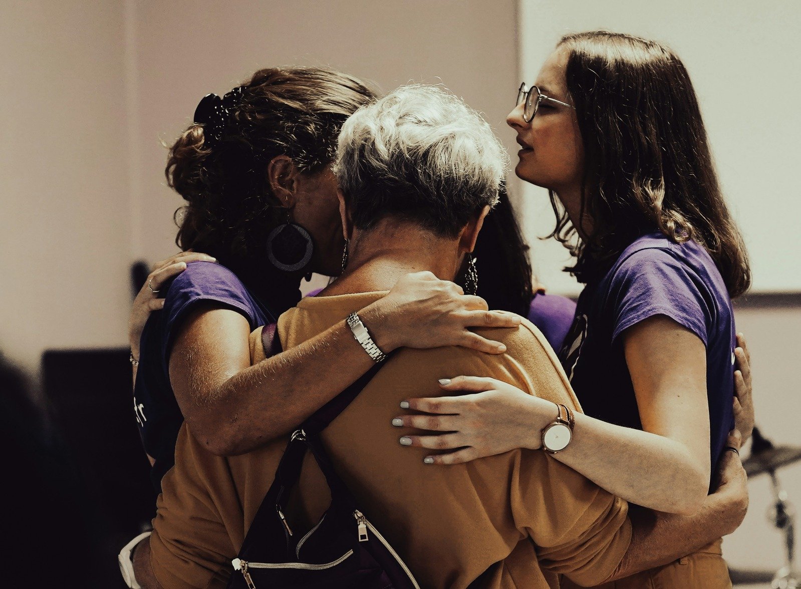 Three members of Cancer Support Netherlands holding one another in a close, supportive embrace